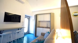 A compact room with a kitchenette, a sofa, a TV, and a dining area. - Grotta Verde Luxury Suite (Capri)
