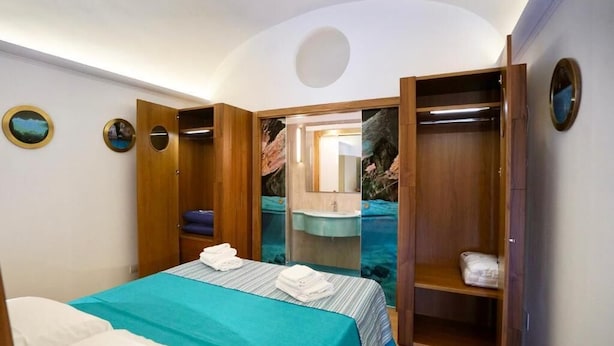 A bedroom with a bed, a wardrobe, a mirror, and a sink. - Grotta Verde Luxury Suite (Capri)