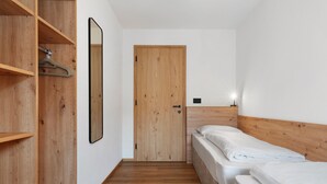 Une petite chambre à coucher, bien rangée, avec une armoire en bois, un lit simple, une porte et un miroir fixé au mur.