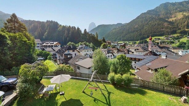 Un quartier résidentiel avec des maisons, une aire de jeux avec des balançoires et une vue sur les montagnes en arrière-plan.