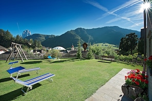 Ein grüner Hinterhof mit Schaukel, Holzfence und Blick auf Berge.