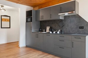 A modern kitchen with grey cabinets, a stainless steel range hood, and a wooden ceiling. - Apartment Verena 1 in the Heart of the Dolomites (Urtijëi)
