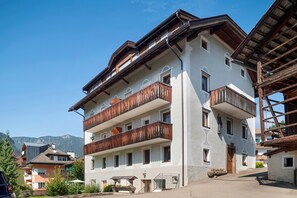Un edifici de diverses plantes amb balcons, una escala de fusta i una muntanya de fons.