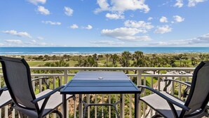 A balcony with a table and chairs overlooking a beach and golf course. - 1368 Shipwatch - Hosted by Moore AI Rentals (Fernandina Beach)