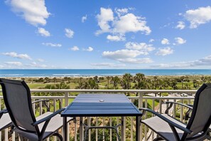 A balcony with a table and chairs overlooking a beach and golf course. - 1368 Shipwatch - Hosted by Moore AI Rentals (Fernandina Beach)