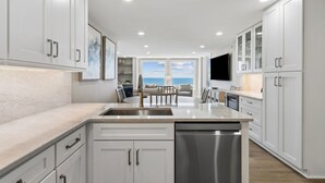 A modern kitchen with white cabinetry, a large island, and a view of the ocean. - 1368 Shipwatch - Hosted by Moore AI Rentals (Fernandina Beach)