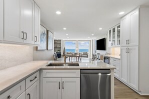 A modern kitchen with white cabinetry, a large island, and a view of the ocean. - 1368 Shipwatch - Hosted by Moore AI Rentals (Fernandina Beach)
