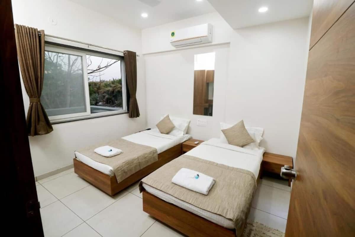 Habitación de hotel con dos camas, una ventana con cortinas, un equipo de aire acondicionado y un espejo en la pared.