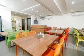 A restaurant with multiple tables and chairs, a counter, and a television screen. - Nova Sahaj Residency (Rajkot)