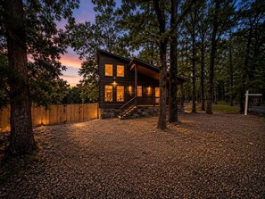 A wooden cabin with a porch, surrounded by trees and a gravel driveway. - Cozy Cabin with Hot Tub & Fire Pit Easy Access to Nearby Lakes and Trails in Broken Bow, Oklahoma (Broken Bow)