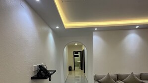 A hallway with a sofa, a phone on a shelf, and a tiled floor. - Al Baida Suites, Rosana Branch (Madinah)