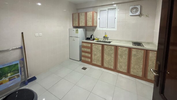 A kitchen with white cabinets, a refrigerator, a sink, and a window. - Al Baida Suites, Rosana Branch (Madinah)