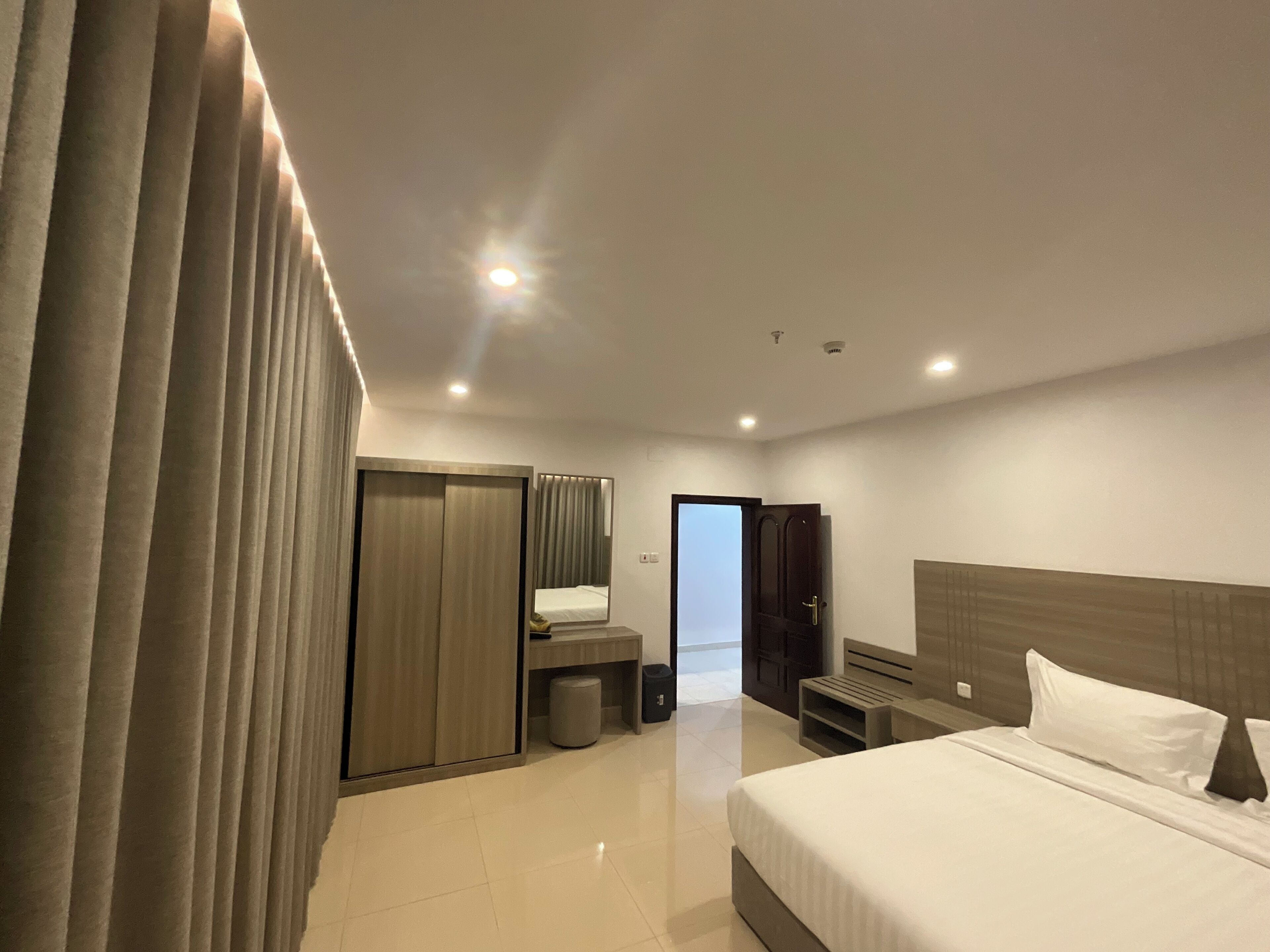 A modern hotel room with a large bed, a wardrobe, a mirror, and a small seating area.