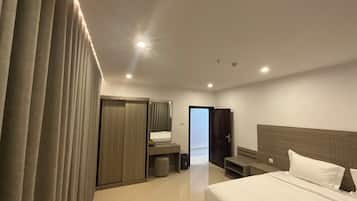 A modern hotel room with a large bed, a wardrobe, a mirror, and a small seating area.