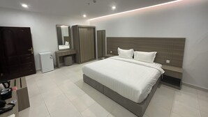 A modern hotel room with a large bed, bedside tables, a wardrobe, a mirror, and a small desk with a chair. - Al Baida Suites, Rosana Branch (Madinah)
