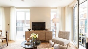 Ein modernes Wohnzimmer mit einem Flachbildfernseher, einem runden Couchtisch, einem bequemen Sessel und einem großen Fenster mit Blick auf die Stadt.