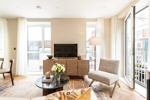 Ein modernes Wohnzimmer mit einem Flachbildfernseher, einem runden Couchtisch, einem bequemen Sessel und einem großen Fenster mit Blick auf die Stadt.