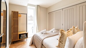Ein Schlafzimmer mit einem Bett, einem Holzschrank, einer Bank, einem Spiegel und einem Fenster mit Vorhängen.