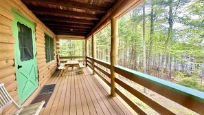 A log cabin with a wooden deck, a green door, and a view of a forest. - Pet-Friendly Waterfront Cabin on Wilson Pond, Maine (Greenville)