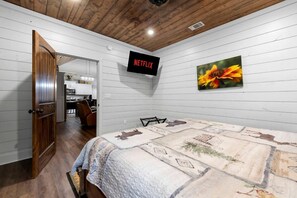 Ein Schlafzimmer mit einem Bett, einem an der Wand montierten Fernseher und einer Tür zu einer Küche.