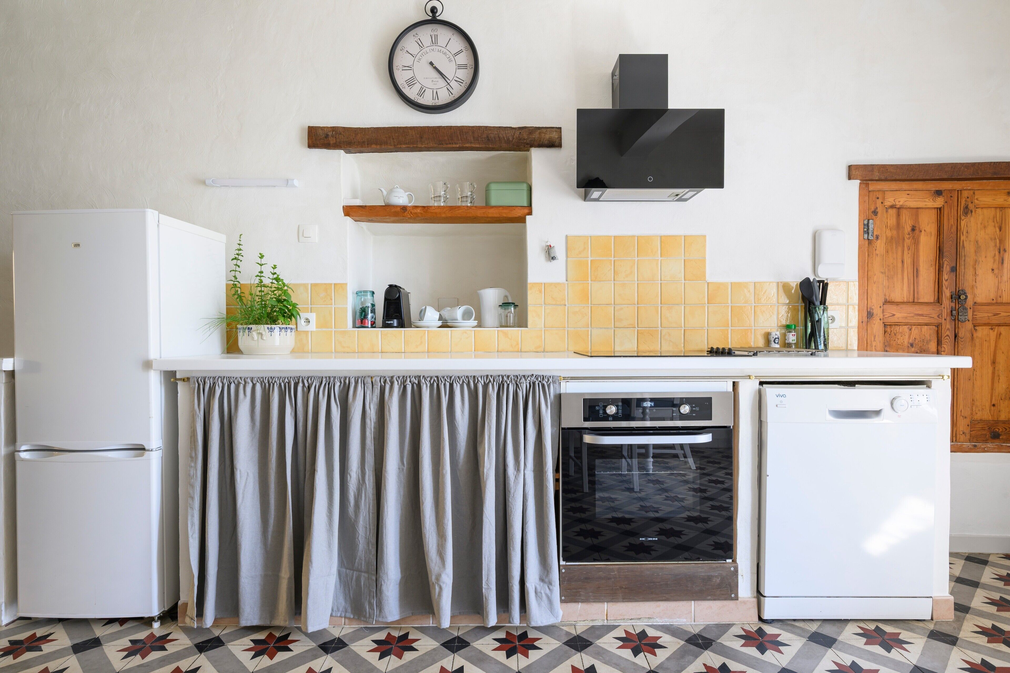 A kitchen with a refrigerator, oven, dishwasher, and a clock on the wall.