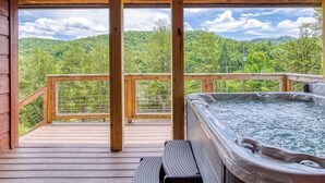 Un terrazzo in legno con una vasca idromassaggio e posti a sedere, con vista su una montagna boscosa.