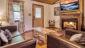 Un accogliente soggiorno con camino, soffitto in legno e televisore a parete.