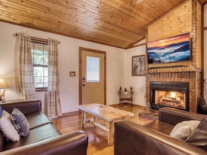 A cozy living room with a fireplace, wooden ceiling, and a television mounted above it. - Rivers Ridge & Guest House - New Listing (Sevierville)