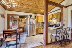 A kitchen with wooden cabinets, a stainless steel refrigerator, a wooden dining table with chairs, and a chandelier. - Rivers Ridge & Guest House - New Listing (Sevierville)