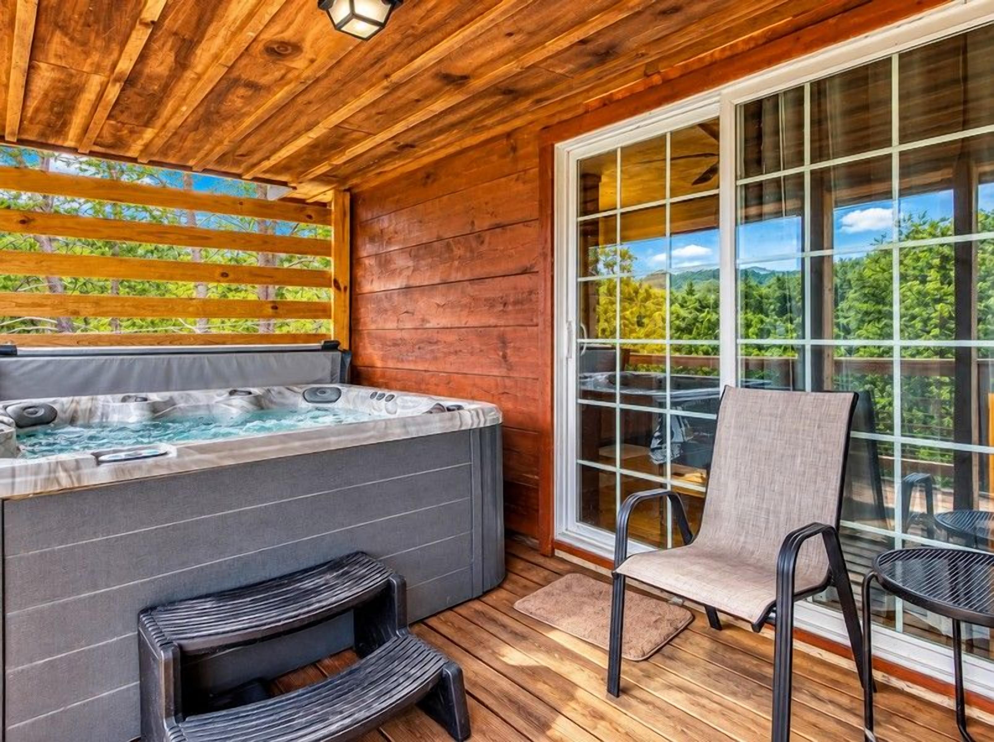 A wooden deck with a hot tub, outdoor seating, and a view of the forest.
