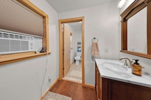A bathroom with a wooden vanity, a mirror, a towel rack, and a toilet visible through an open door. - Moose Hollow Studio Cabin (Eureka)