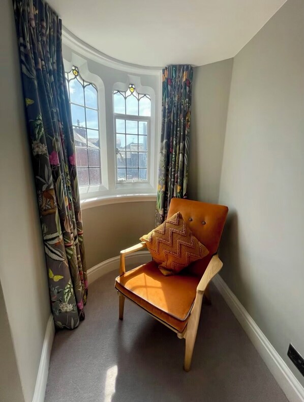 A corner room with a window, a chair with a cushion, and floral curtains. - Beautiful 2 bed cottage (Chester)