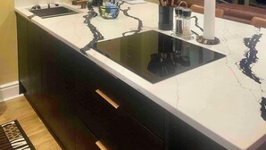 Eine moderne Küche mit einer Marmorinsel, Pendelleuchten, einem gerahmten Kunstwerk und einem Kamin.