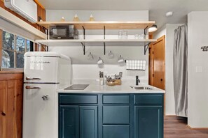 Eine Küche mit Kühlschrank, Mikrowelle und Spüle. Es gibt Schränke und eine Arbeitsplatte mit verschiedenen Küchenutensilien.
