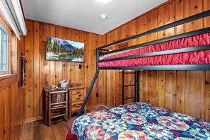 A bunk bed room with wooden walls, a desk with drawers, a chair, and a painting of a mountain landscape. - Inviting Rustic Cabins with Outdoor Gathering Areas near Garden of the Gods in Colorado Springs, Colorado (Colorado Springs)