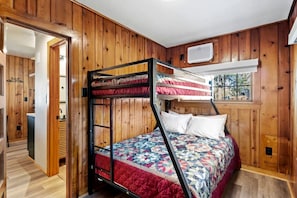 Ein Stockbett mit Bettdecke, Holzwände, einem Fenster und einer Tür zu einem Badezimmer.