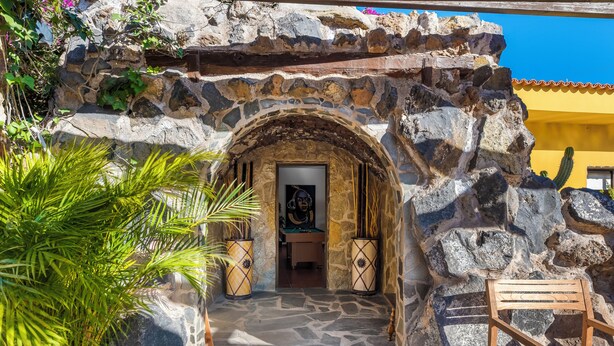 Un portale ad arco in pietra che dà accesso a un edificio, con una sedia di legno sulla destra.
