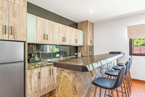 A kitchen with a stone island, bar stools, and a refrigerator. - Finca Ifaya, a private lodging located on a beautiful and peaceful estate (San Miguel)