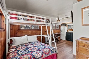 Ein Stockbett mit einer Decke, eine Leiter, ein kleiner Tisch mit Stühlen, eine Küchenzeile und Holzwände.