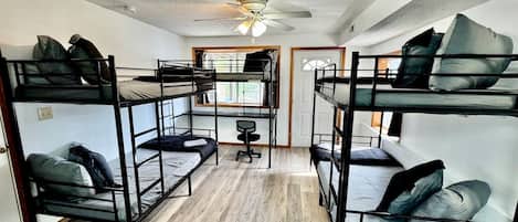 A dormitory room with bunk beds, a ceiling fan, and a window.
