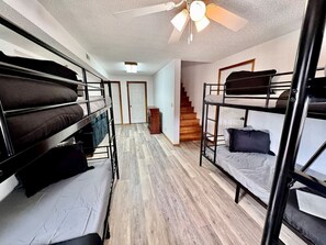 Ein Schlafraum mit Etagenbetten, Deckenventilator und einer Treppe zu einer weiteren Ebene.