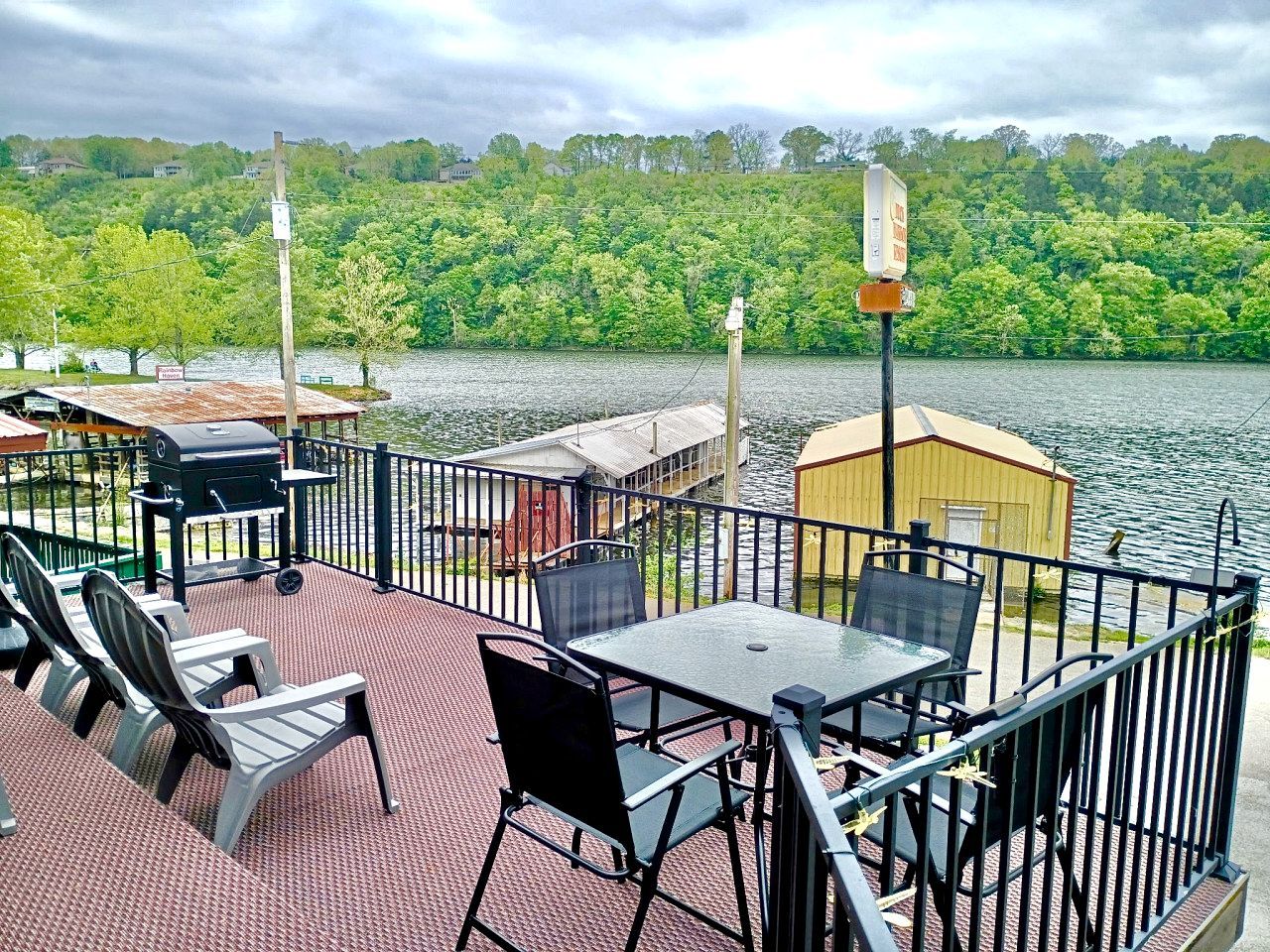 A deck with outdoor seating, a grill, and a small shed by a lake.