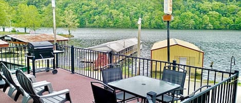 A deck with outdoor seating, a grill, and a small shed by a lake.