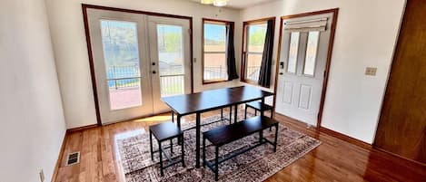 A room with a wooden floor, a ceiling fan, a dining table with benches, and a patterned rug.