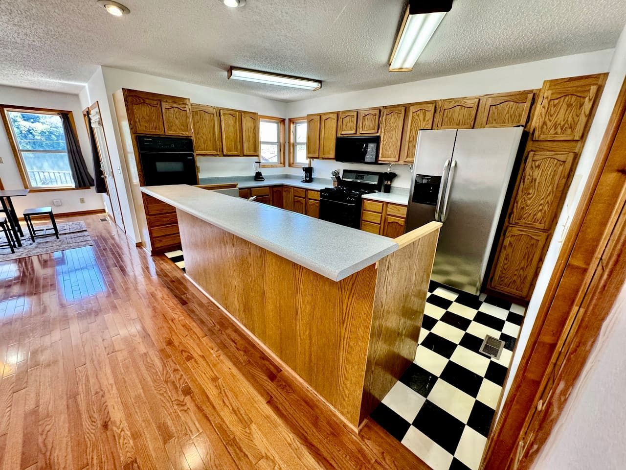 A kitchen with wooden cabinets, a central island, and a black and white checkered floor.