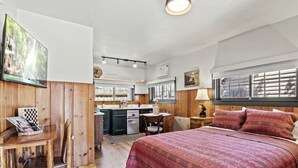 Une pièce confortable comprenant un lit, un bureau, une chaise, un petit coin cuisine et une fenêtre avec des stores.