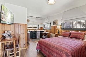 A cozy room with a bed, a desk, a chair, a small kitchen area, and a window with blinds. - Trailside Cabin Escape with Stunning Views and Easy Adventure Access in Colorado Springs, Colorado (Colorado Springs)