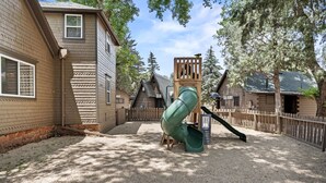 Une aire de jeux avec un toboggan, entourée de structures et de maisons en bois destinées aux jeux.