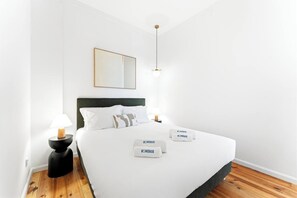 Ein schlichtes Hotelzimmer mit einem Bett, zwei Nachttischlampen, einem Nachttisch, einem wandmontierten Spiegel und einem gerahmten Bild.