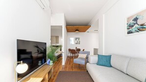En moderne stue med et fladskærms-tv, en sofa, et spisebord og et træloft.